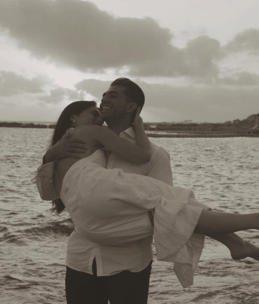 Kyriakos carrying Maria in his arms by the water, both laughing